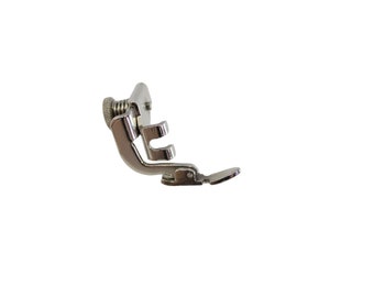 May include: A silver sewing machine foot with a spring-loaded adjustment screw. The foot has a curved shape and a small, flat plate on the bottom.