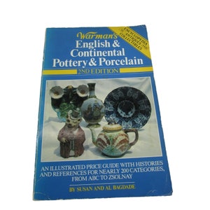 May include: The cover of a book titled "Warman's Encyclopedia of Antiques and Collectibles: English & Continental Pottery & Porcelain, 2nd Edition". The cover features a blue background with a variety of colourful pottery and porcelain pieces, including a teapot, a vase, and a plate.