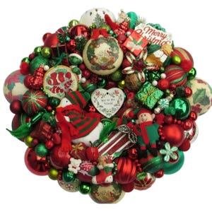 May include: A Christmas ornament arrangement with red and green baubles, decorative elements, and small figurines. Includes a snowman, elf, and heart-shaped ornament with the text "Joy to the World".