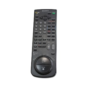 Puede incluir: Un mando a distancia negro Sony para VCR con un bot&oacute;n circular en el centro. El bot&oacute;n tiene un s&iacute;mbolo de reproducci&oacute;n y un bot&oacute;n de parada. El mando a distancia tiene una variedad de botones, incluidos los botones de canal arriba y abajo, volumen arriba y abajo, y un bot&oacute;n de pausa.