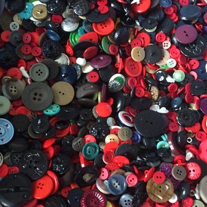 May include: A large collection of colorful buttons in various shapes, sizes, and materials. The buttons are mostly red, black, and white, with some green, blue, and brown buttons. The buttons are arranged in a random pattern, creating a visually appealing and textured surface.