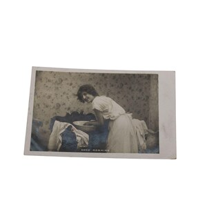 Peut inclure: Carte postale vintage en noir et blanc représentant une femme en robe blanche se lavant dans un bol. La carte postale porte l'inscription "GOOD MORNING" en bas. L'arrière-plan présente un motif floral.