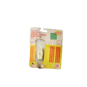 May include: A white plastic miniature feed-thru switch with yellow and red stripes on the packaging. The packaging also has the text "MINIATURE KWIK-WIRI FEED THRU SWITCH" and "SERVESS".