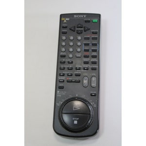 Puede incluir: Un mando a distancia negro Sony para VCR con una variedad de botones y una almohadilla de control circular con botones de reproducci&oacute;n, parada y pausa. El mando a distancia tiene el texto "SONY" en la parte superior.