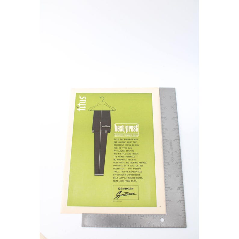 May include: An advertisement for "best prest" trousers by Oshkosh Sportswear. The image features a pair of dark trousers hanging on a hanger against a green background. Text includes "titus" and "slim leg from $5.95."