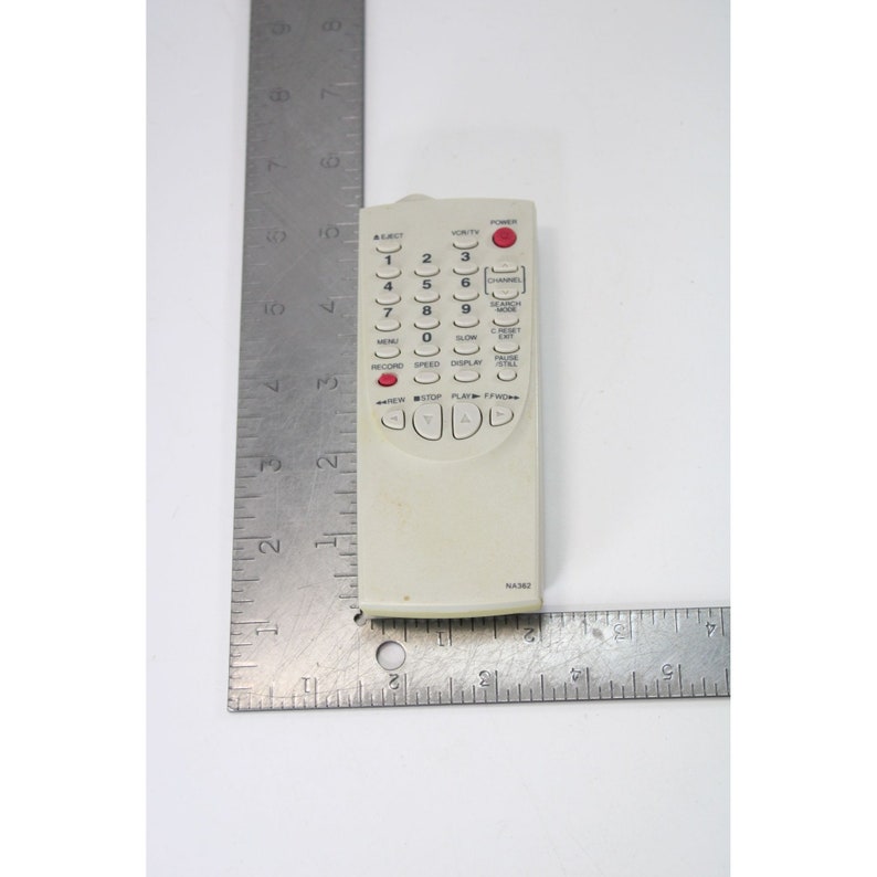 May include: A white remote control with a red button labeled "Power". The remote has a number pad, directional buttons, and buttons for "Menu", "Record", "Speed", "Display", "Clock", "Direct", "Pause", "Exit", "Channel", "Blanket Mode", "Volume", and "A/Select". The remote has the model number "NA362" printed on the bottom.