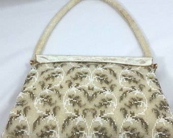 May include: A white beaded handbag with a gold and white floral pattern. The bag has a white beaded handle.
