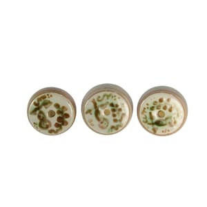 May include: Three ceramic cabinet knobs with a floral design. The knobs have a cream-colored top with brown and green floral patterns. The sides are a light brown color. Each knob has a small hole in the center.