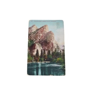 Könnte beinhalten: Vintage Postkarte mit einer malerischen Ansicht des Yosemite-Tals, Kalifornien. Das Bild zeigt hoch aufragende Felsformationen, üppig grüne Bäume und einen ruhigen Fluss, der den Himmel widerspiegelt. Die Postkarte hat ein leicht gealtertes Aussehen.