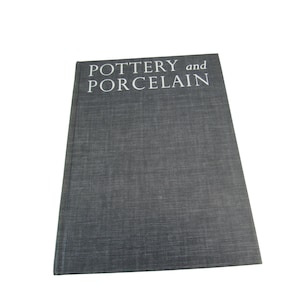 May include: A hardcover book titled "POTTERY and PORCELAIN" with a dark gray textured cover. The book is closed and positioned at a slight angle, showcasing the title in white capital letters. The background is plain white.
