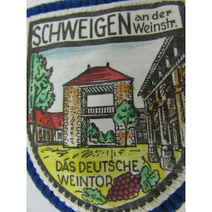 May include: A patch with a shield design featuring a brick tower with a red roof, trees, and buildings. The text "SCHWEIGEN" and "an der Weinstr." are at the top, and "DAS DEUTSCHE WEINTOR" is at the bottom, with a grape cluster and leaves.