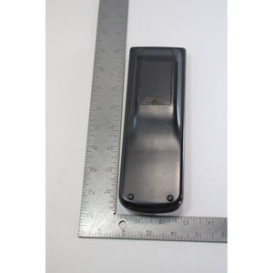 Puede incluir: Mando a distancia negro con una peque&ntilde;a flecha apuntando hacia arriba en la parte superior. El mando a distancia mide aproximadamente 15 cm de largo.