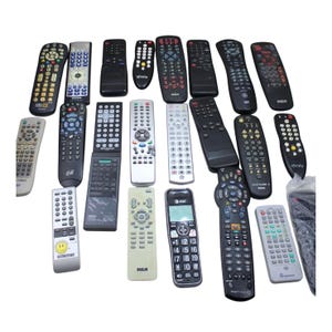 Könnte beinhalten: Eine Sammlung von 20 verschiedenen Fernbedienungen, hauptsächlich schwarz, mit einigen silbernen und weißen Akzenten. Die Fernbedienungen sind in Reihen und Spalten angeordnet, wobei sich einige Fernbedienungen überlappen. Einige der Fernbedienungen haben Tasten mit Text, wie "xfinity" und "finity".