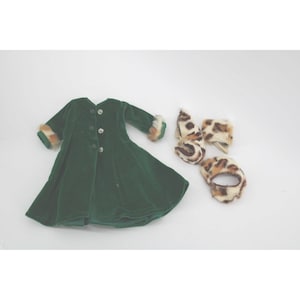 May include: A green velvet coat with button closures and faux fur trim on the cuffs. The coat is paired with a matching set of faux fur accessories, including a hat, scarf, and a wristband.