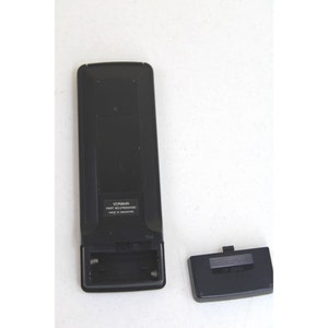 May include: Black remote control with a battery compartment open, revealing two AA batteries. The remote has the text "VCR964N PART NO. L7050304R01 MADE IN SINGAPORE" printed on it. The battery cover is separate and black.
