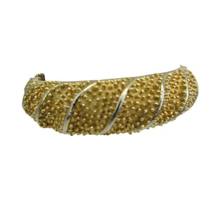 May include: A gold-toned, textured, open bangle bracelet with a twisted design.