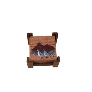 May include: Set of four wooden coasters with a painted design of quail birds on a brown background. The coasters are in a wooden holder.