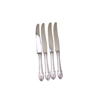 Op de afbeelding: Vier zilveren dinermessen met sierlijke handvatten.