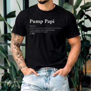 May include: A black t-shirt with white text that reads "Pump Papi" and a definition of the slang term. The definition includes the words "cool, confident, influential, good looking, embodiment of swagger, and me."