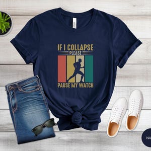 May include: Navy blue t-shirt with a vintage-style graphic that says "If I Collapse Please Pause My Watch". The graphic features a runner in a retro style.