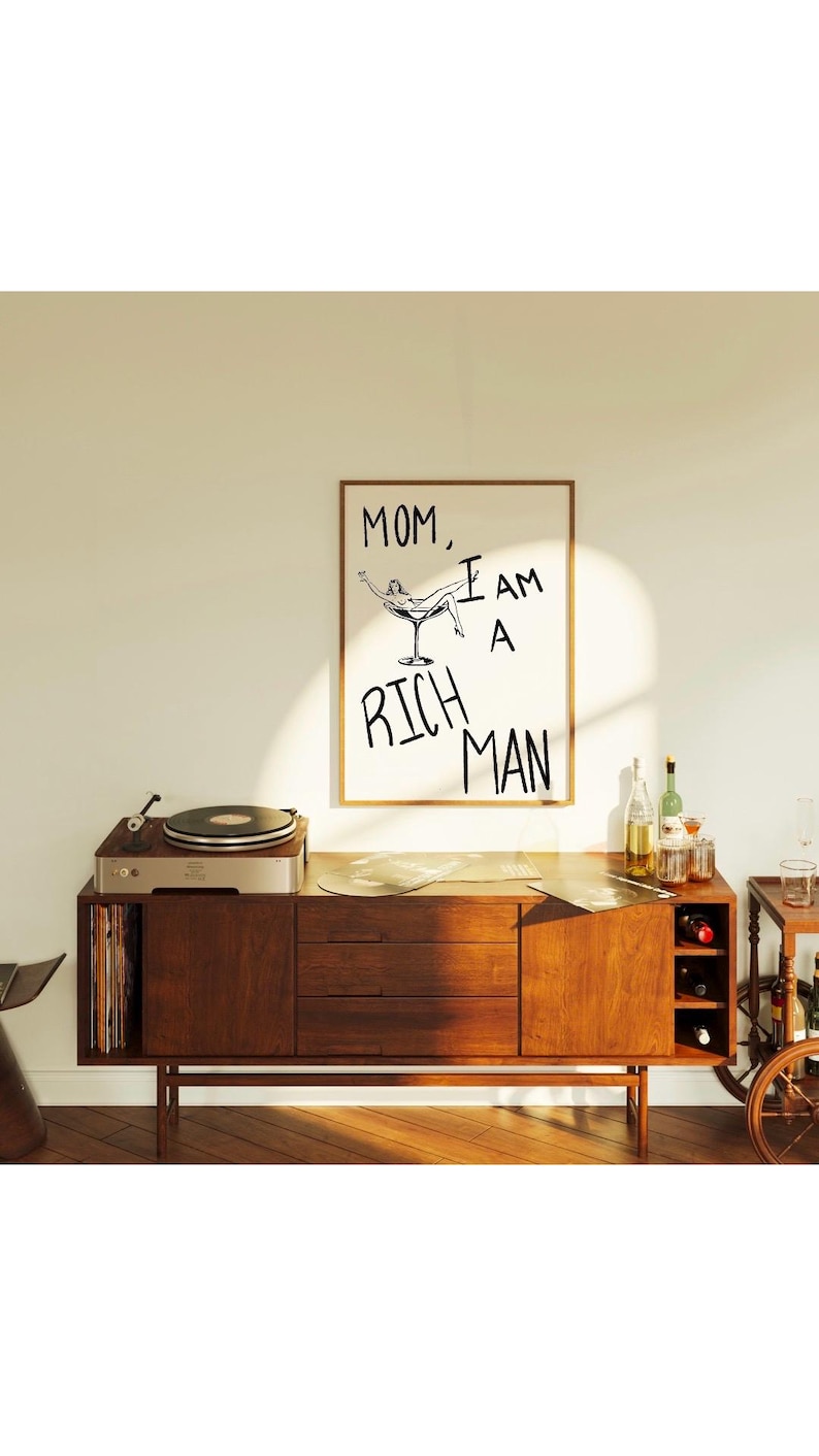 May include: A framed print with a black and white illustration of a woman reclining in a martini glass. The text "MOM, I AM A RICH MAN" is written in black below the illustration.