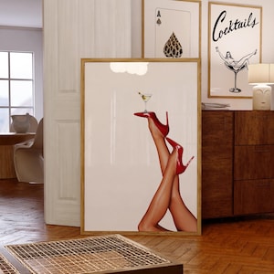 May include: A framed print of a pair of legs in red high heels holding a martini glass with an olive. The background is white.