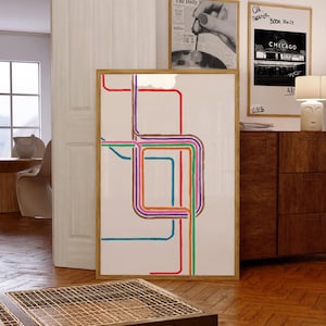 May include: A framed abstract art print featuring a colorful, geometric design of interconnected lines in red, blue, green, orange, and purple against a white background. The artwork is displayed in a room with other framed prints and wooden furniture.
