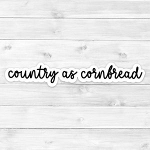 May include: A white sticker with the phrase "country as cornbread" in black cursive font. The sticker is set against a white wooden background.