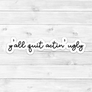 May include: White wood background with a black and white sticker that says "y'all quit actin' ugly"