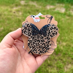 May include: A black and gold glitter Minnie Mouse ear headband with a leopard print design.
