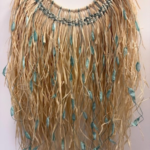 May include: A circular woven wall hanging, crafted from natural straw with a fringed lower section. Teal-coloured accents and dangling embellishments are incorporated. The piece has a textured, organic design, suitable for bohemian or coastal interior styles.
