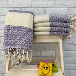 May include: A stack of purple and white striped towels with a fringe border. The towels are folded and stacked on a wooden stool.