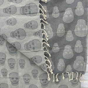 May include: Two gray cotton towels with a skull pattern. The towels are fringed and have a white background.