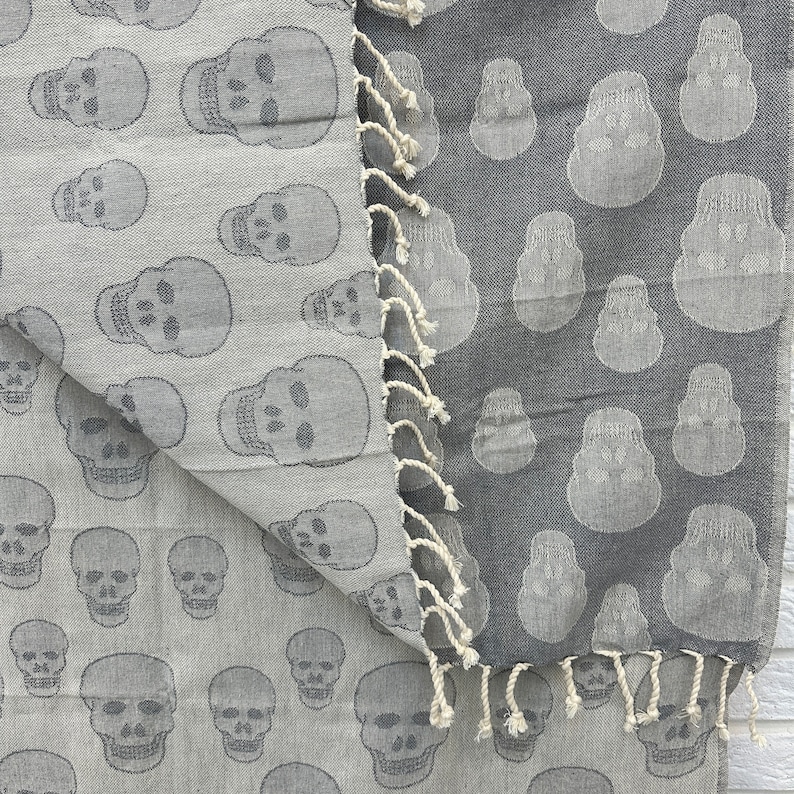 May include: Two gray cotton towels with a skull pattern. The towels are fringed and have a white background.