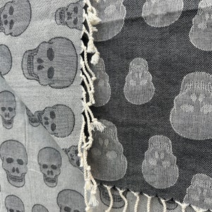 May include: A black and white patterned fabric with a skull design. The fabric has a fringe border.
