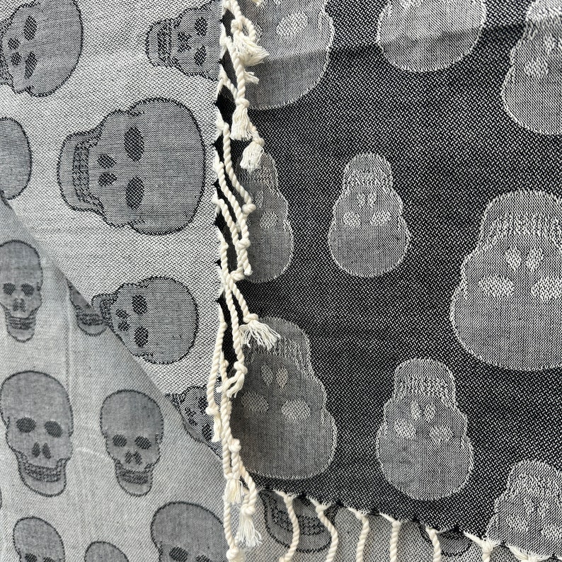 May include: A black and white patterned fabric with a skull design. The fabric has a fringe border.
