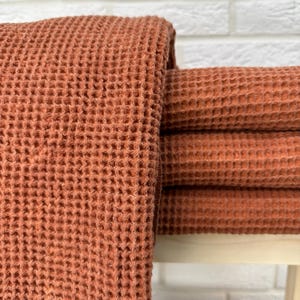 May include: A stack of four waffle weave towels in a terracotta orange color. The towels are folded and stacked on a white surface.