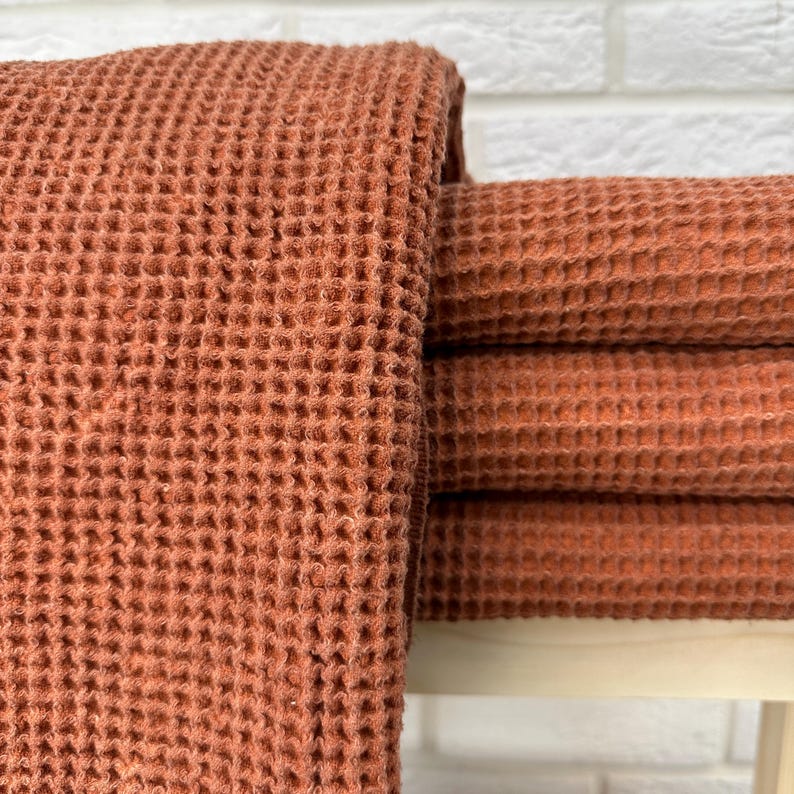 May include: A stack of four waffle weave towels in a terracotta orange color. The towels are folded and stacked on a white surface.