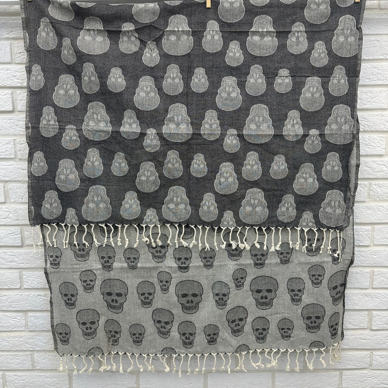 May include: A black and white patterned throw blanket with a skull design. The blanket has a fringe border and is made of a soft, woven fabric.