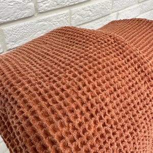 May include: A close-up of a waffle weave fabric in a terracotta color. The fabric has a textured, waffle-like pattern.