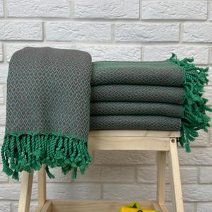 May include: A stack of green and burgundy patterned towels with green fringe. The towels are folded and stacked on a wooden shelf.