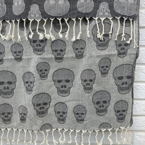 May include: A gray and white patterned fabric with a fringe border. The fabric features a repeating pattern of black skull designs.