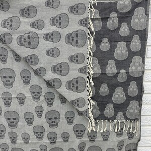 May include: A reversible gray and black cotton throw blanket with a skull pattern. The blanket is fringed on all sides.