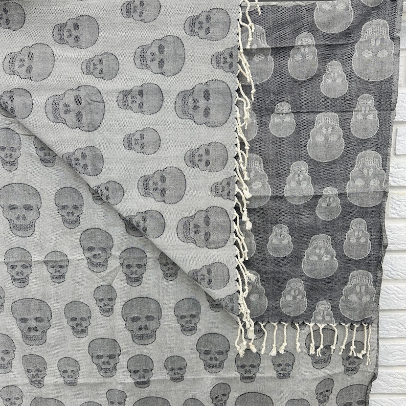 May include: A reversible gray and black cotton throw blanket with a skull pattern. The blanket is fringed on all sides.