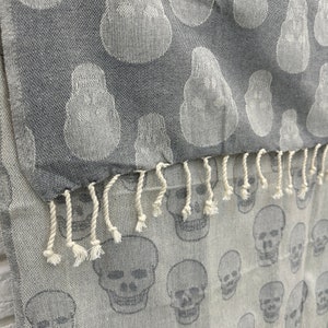 May include: Gray and white patterned fabric with a fringe. The fabric has a skull design.