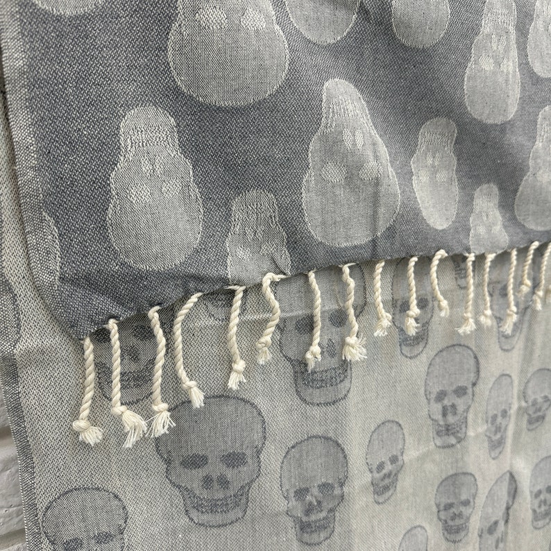 May include: Gray and white patterned fabric with a fringe. The fabric has a skull design.