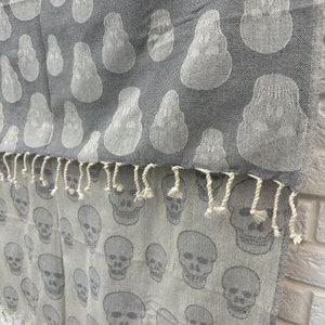 May include: A gray and white woven throw blanket with a skull pattern. The top half of the blanket features a gray background with a white skull pattern. The bottom half of the blanket features a white background with a gray skull pattern.