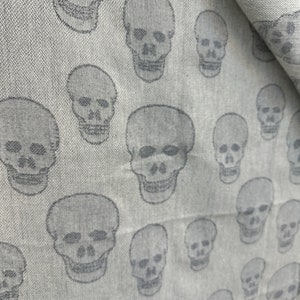 May include: A white fabric with a repeating pattern of gray skull silhouettes.