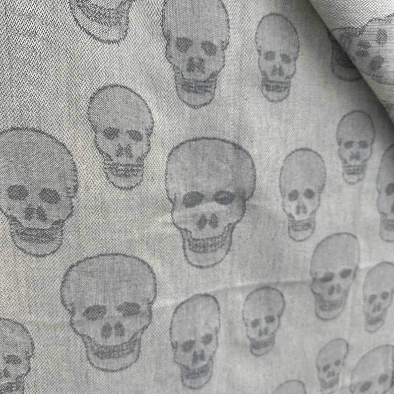 May include: A white fabric with a repeating pattern of gray skull silhouettes.