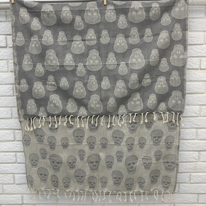 May include: Gray and white cotton throw blanket with a skull pattern. The blanket has fringe on the bottom edge.